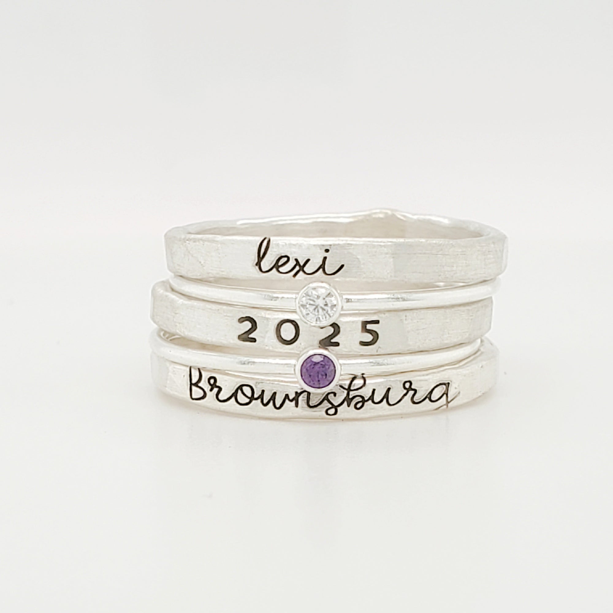 A set of three stackable rings made of yellow gold, with two gemstones, and personalized engravings including 'BROWNSBURG', 'class of 2025' and 'MAREN'.