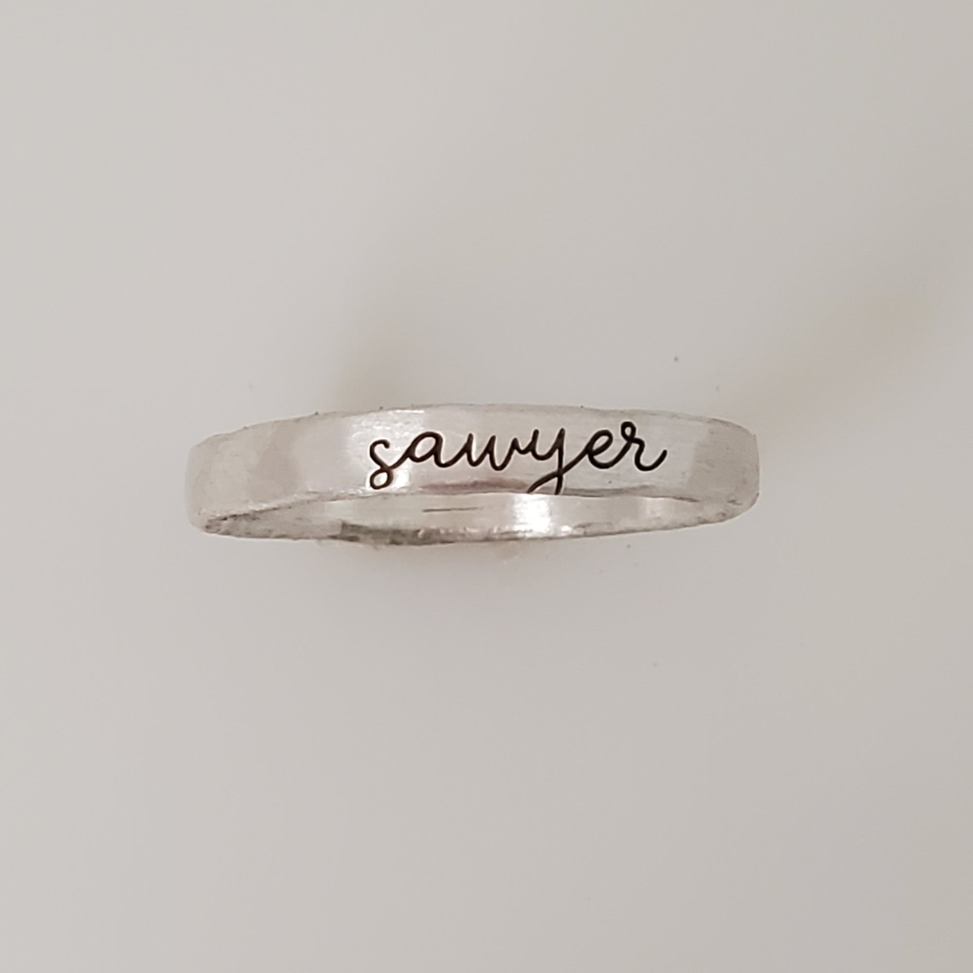 A silver stacking ring with the name 'sawyer' engraved on it, displayed against a white background.