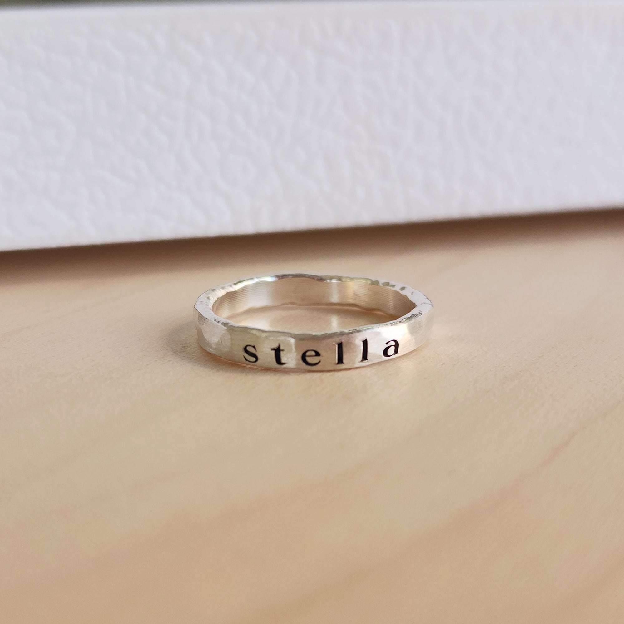 A sterling silver personalized stacking ring with the name 'amelia' engraved on it, displayed on a wooden surface.