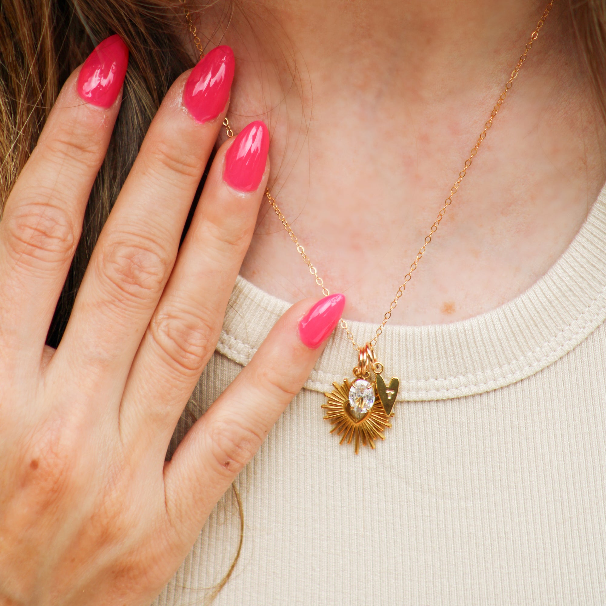 Gold necklace with a pendant worn by a person with pink nail polish.