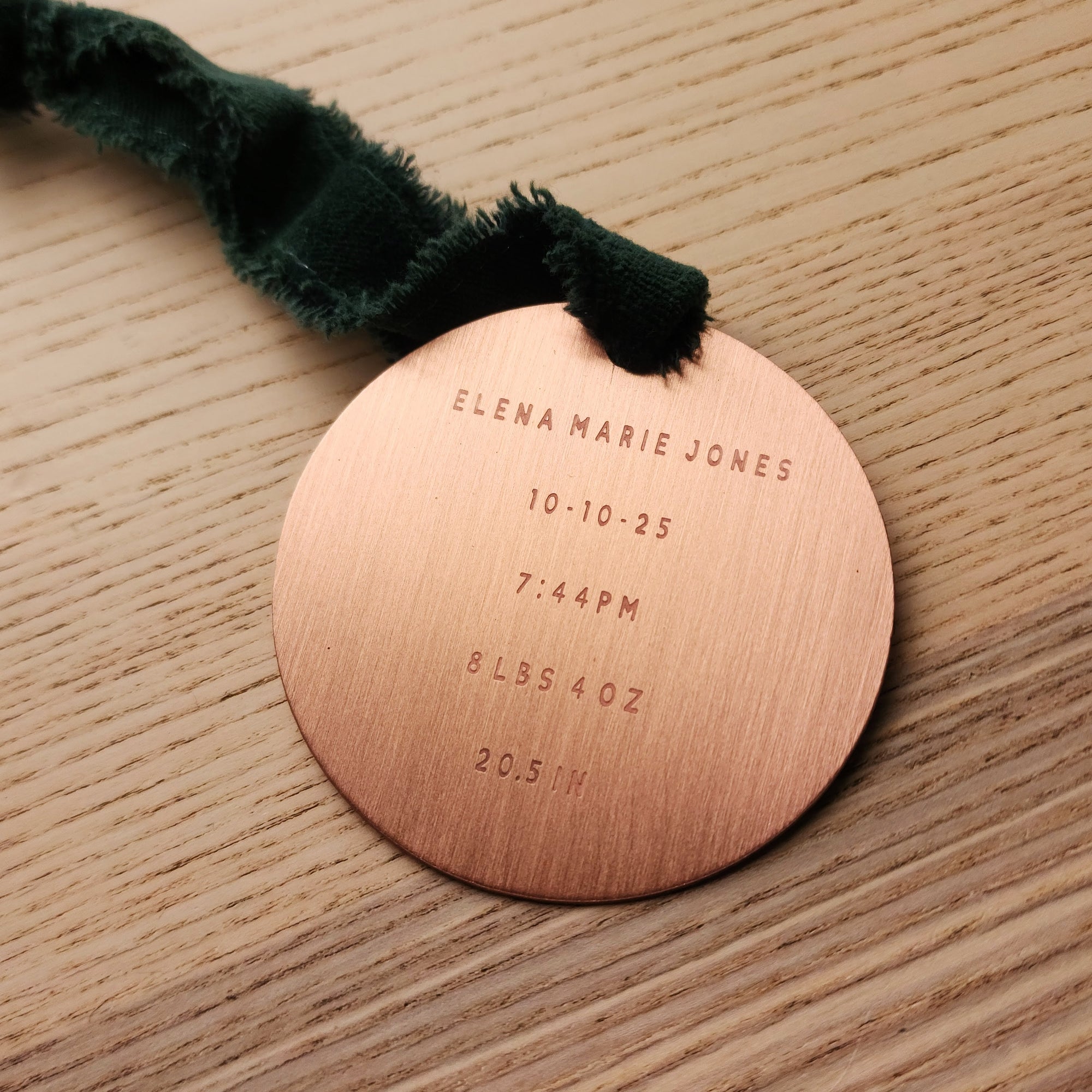 Copper baby birth announcement ornament with engraved details on a wooden surface