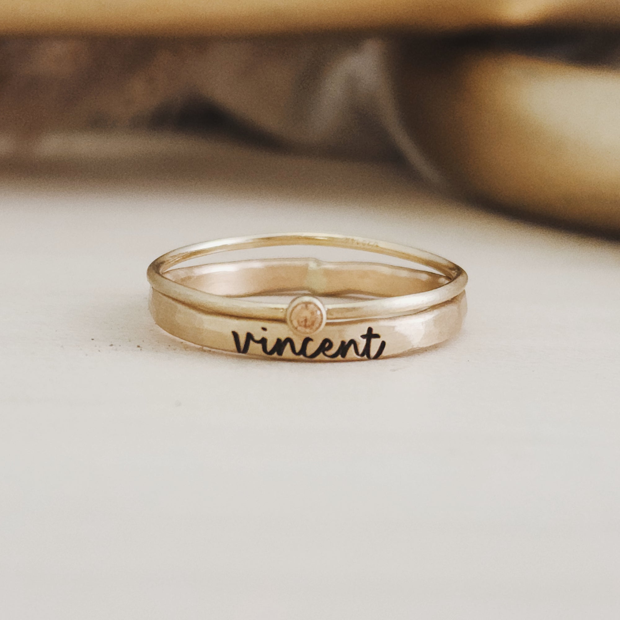 A gold-filled stacking ring set with one ring displaying the name 'Vincent' engraved on it, placed against a neutral background.
