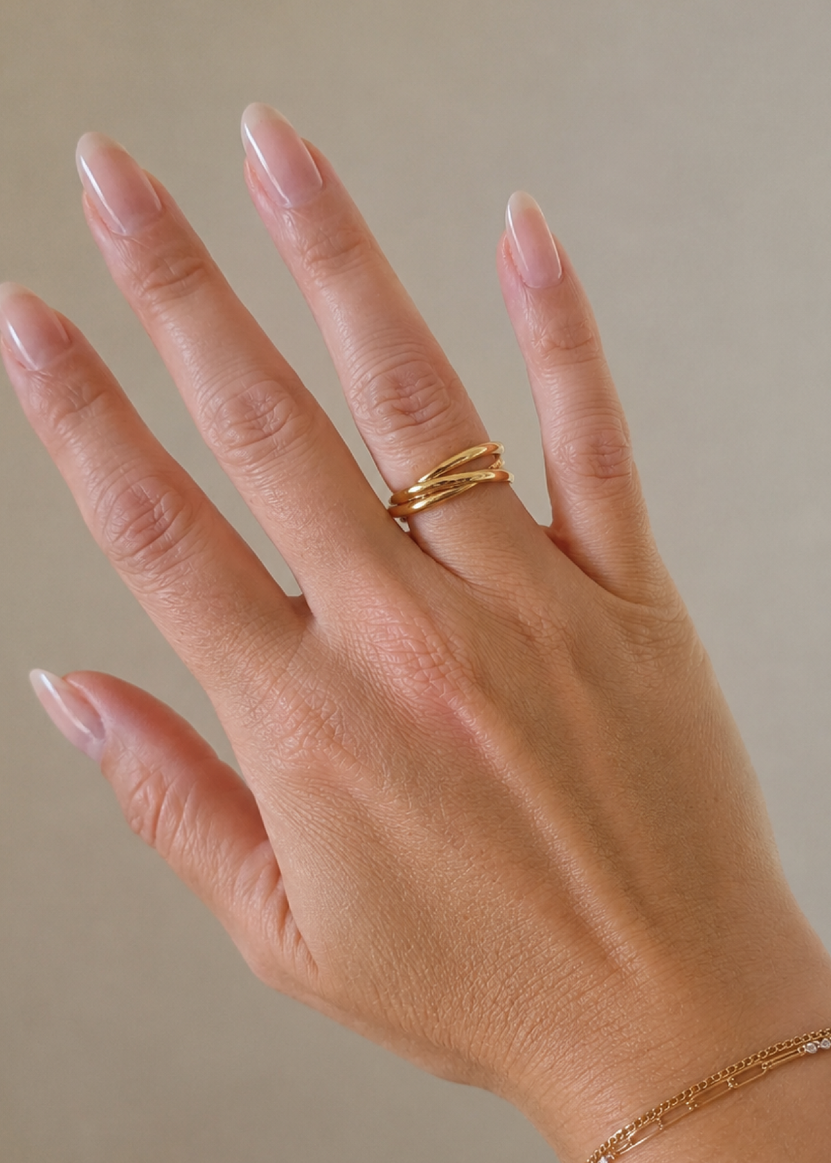Hand wearing a gold ring on a neutral background