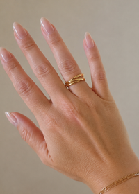 Hand wearing a gold ring on a neutral background