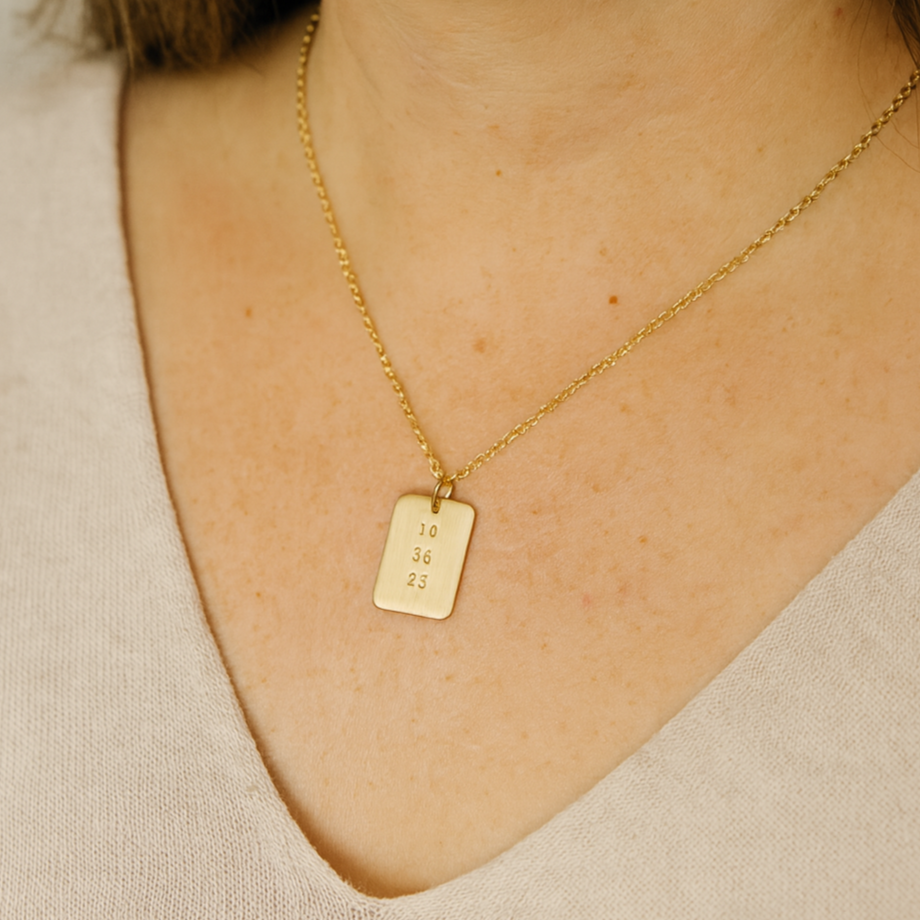 Woman wearing gold date-stamped pendant necklace with gold chain against a neutral top