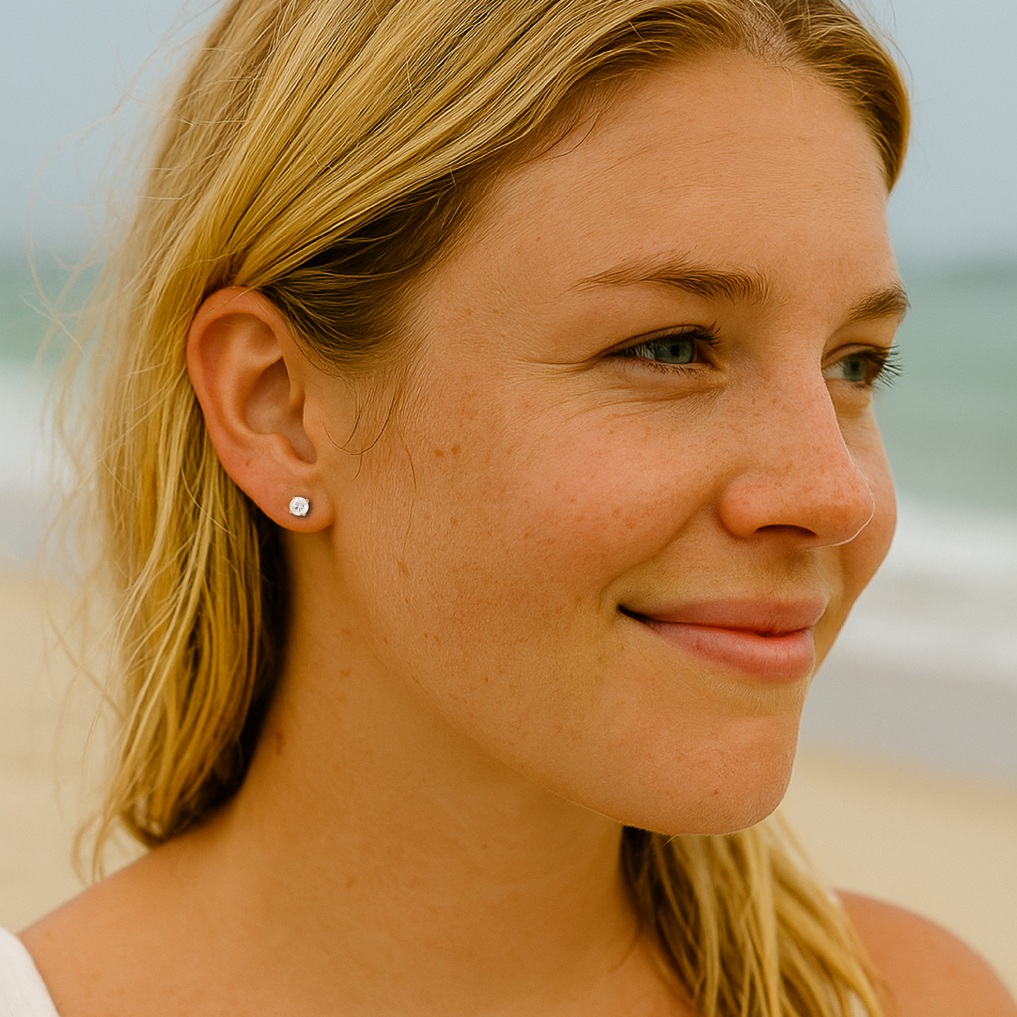 Close-up of a woman with blonde hair and earrings on a beach.
