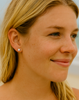 Close-up of a woman with blonde hair and earrings on a beach.