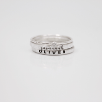A set of three rings, including two name rings in different fonts and a clear birthstone ring, displayed against a white background.