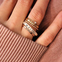 Close-up of a hand wearing a personalized custom ring set with names and designs, showcasing sterling silver and gold rings.