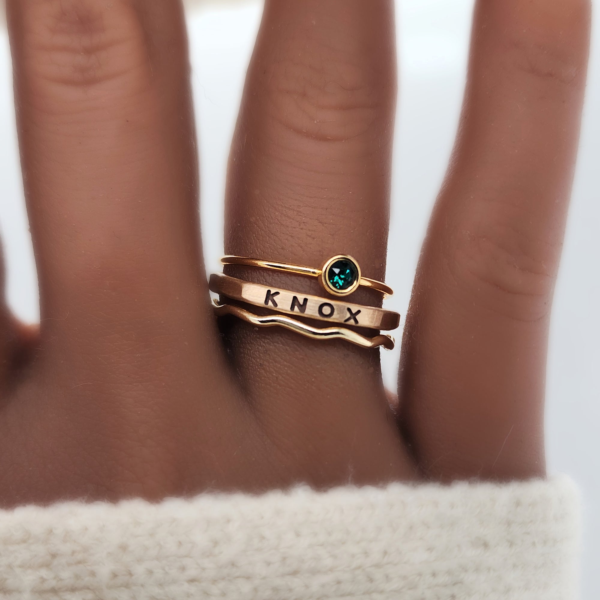 A set of three golden rings, featuring a birthstone, a name ring, and a wavy ring 